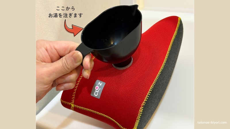 クロッツの湯たんぽに、専用の漏斗をセットしてお湯を注ごうとしている様子。赤いウェットスーツ素材の本体と黒い漏斗のコントラスト